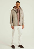 Hellgraue Jacke mit zwei Fronttaschen über einem rosa Kapuzenpullover. Weiße Hosen und dunkelbraune Schuhe vervollständigen das Outfit.