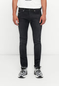 Mann in slim-fit schwarzen Jeans und schwarz-weißen Sportschuhen, der vor einem weißen Hintergrund steht.