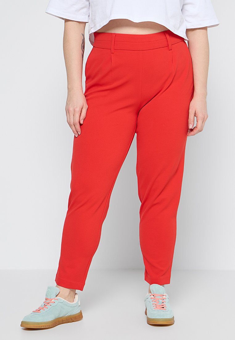 Rote, schmal zulaufende Hose aus einem dehnbaren Stoff, mit Seitentaschen und einer glatten Oberfläche, kombiniert mit hellblauen Sneakers.