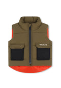 Gepolsterte Weste mit hohem Kragen, olivgrüner Hauptkörper, orangefarbener unterer Saum, schwarze Taschen und Frontreißverschluss. Timberland-Logo auf der Brust.