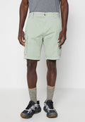 Mann trägt hellgrüne Cargo-Shorts, ein graues T-Shirt, grau-beige Socken und schwarze, graue sowie weiße Sneaker und steht vor einem schlichten Hintergrund.