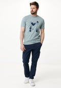 Hellblaues T-Shirt mit kurzen Ärmeln, das ein dunkelblaues Grafikdesign zeigt. Getragen mit marineblauen Cargohosen und weißen Sneakers. Einfaches, lässiges Outfit.