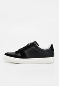 Schwarzer Sneaker mit weißer Sohle, Schnürverschluss vorne und dezenten Perforationen an Zehen- und Seitenpartien.