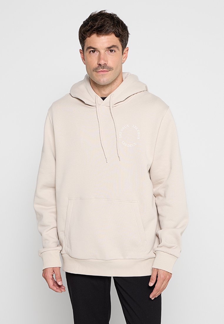Beige Kapuzenpullover mit einer Fronttasche, gerippten Bündchen und Saum sowie einem Logodetail auf der Brust. Hergestellt aus einem weichen, strukturierten Stoff.