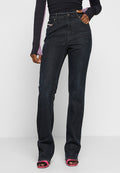 Model trägt schwarze, hochtaillierte, gerade geschnittene Jeans, ein langärmliges Oberteil in Schwarz und Lila sowie pinkfarbene Sandalen mit offener Spitze und schwarzen Netzstrümpfen.