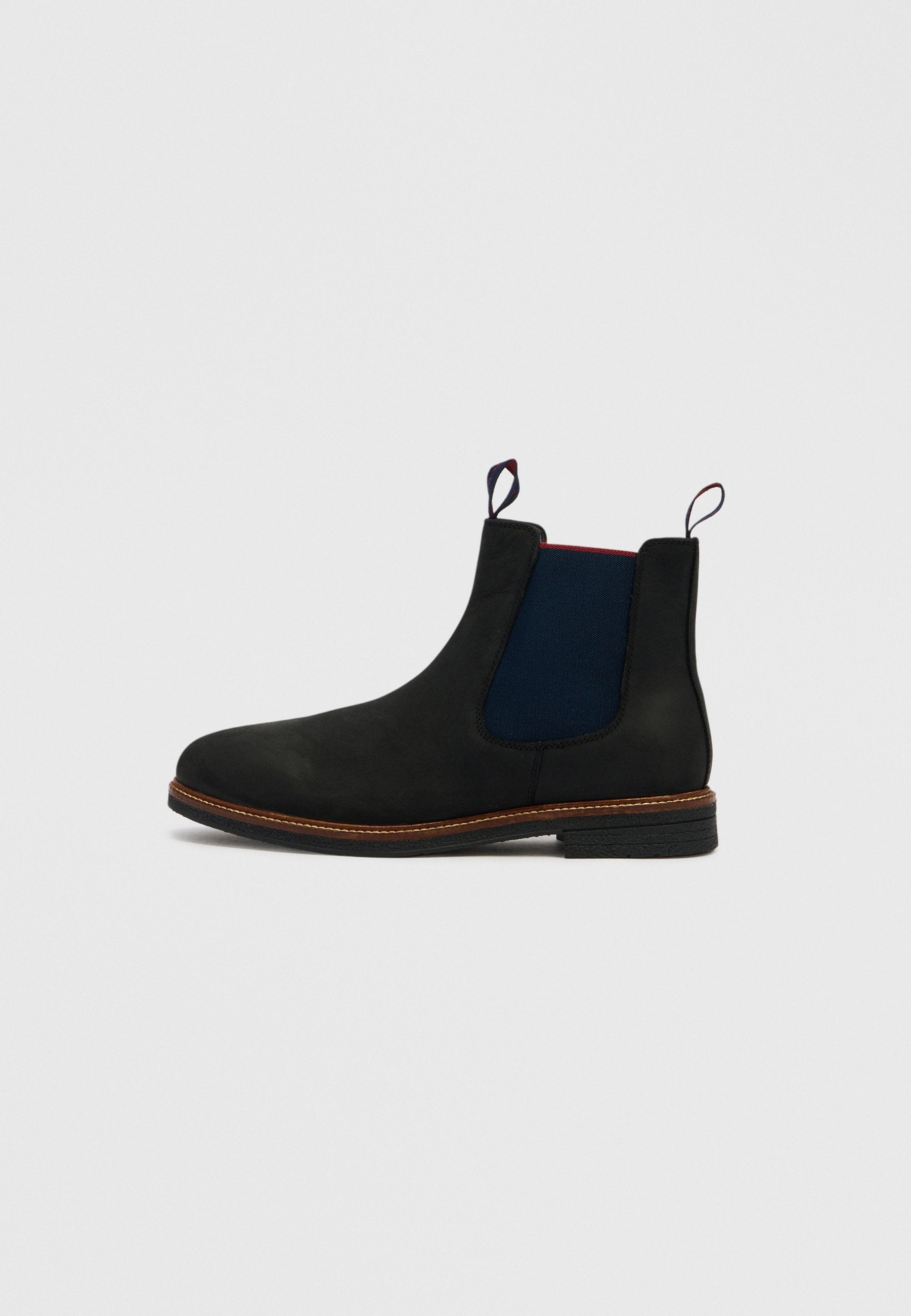 Schwarzer Chelsea-Stiefel mit marineblauen seitlichen Elastikeinsätzen, brauner Kappnaht, Zuglaschen vorne und hinten sowie niedrigem, gestapeltem Absatz auf weißem Hintergrund.