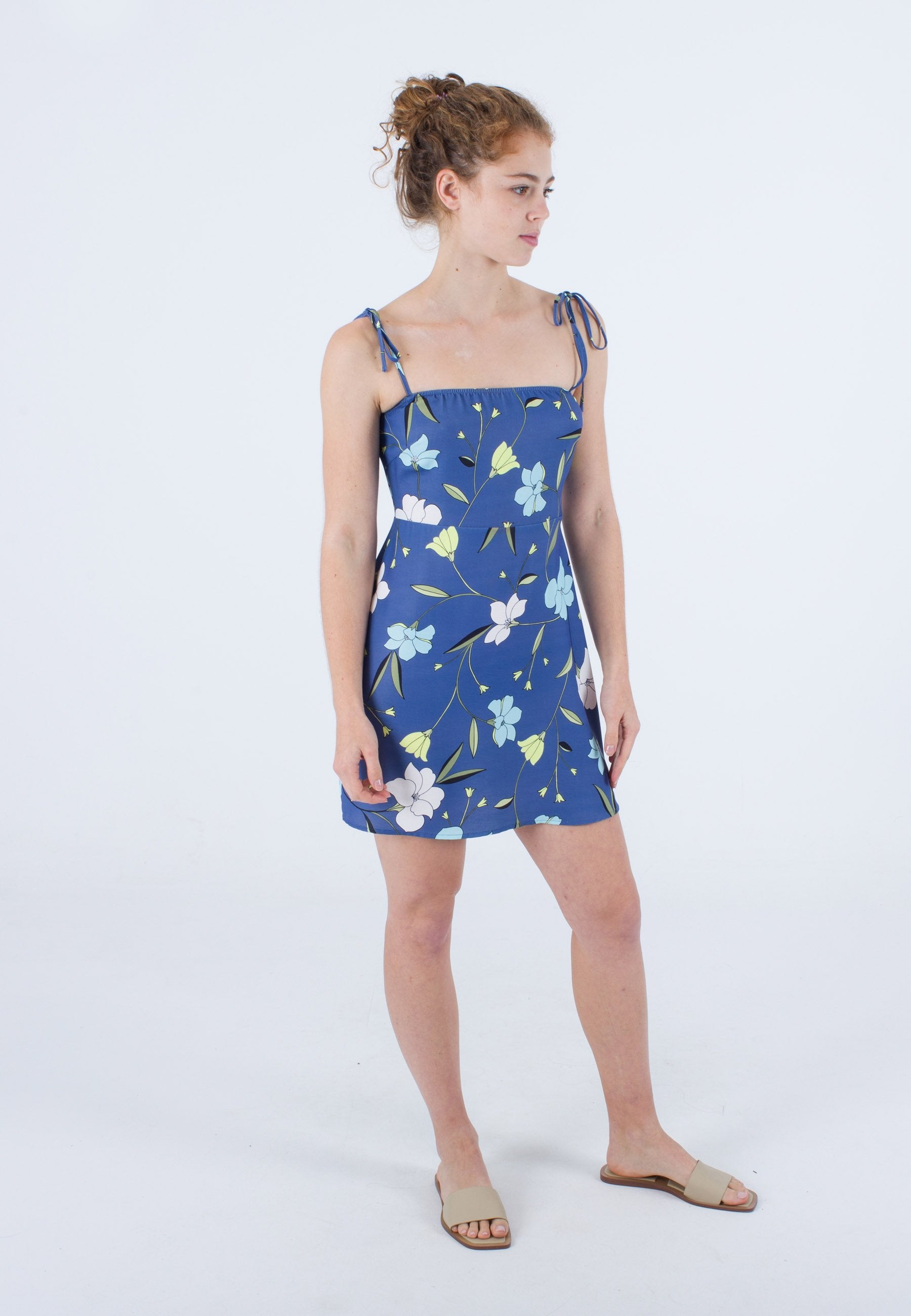 Kurzes blaues Kleid mit floralem Muster in Weiß und Grün, verstellbaren Bindeträgern und passgenauem Oberteil, sitzt oberhalb der Knie.