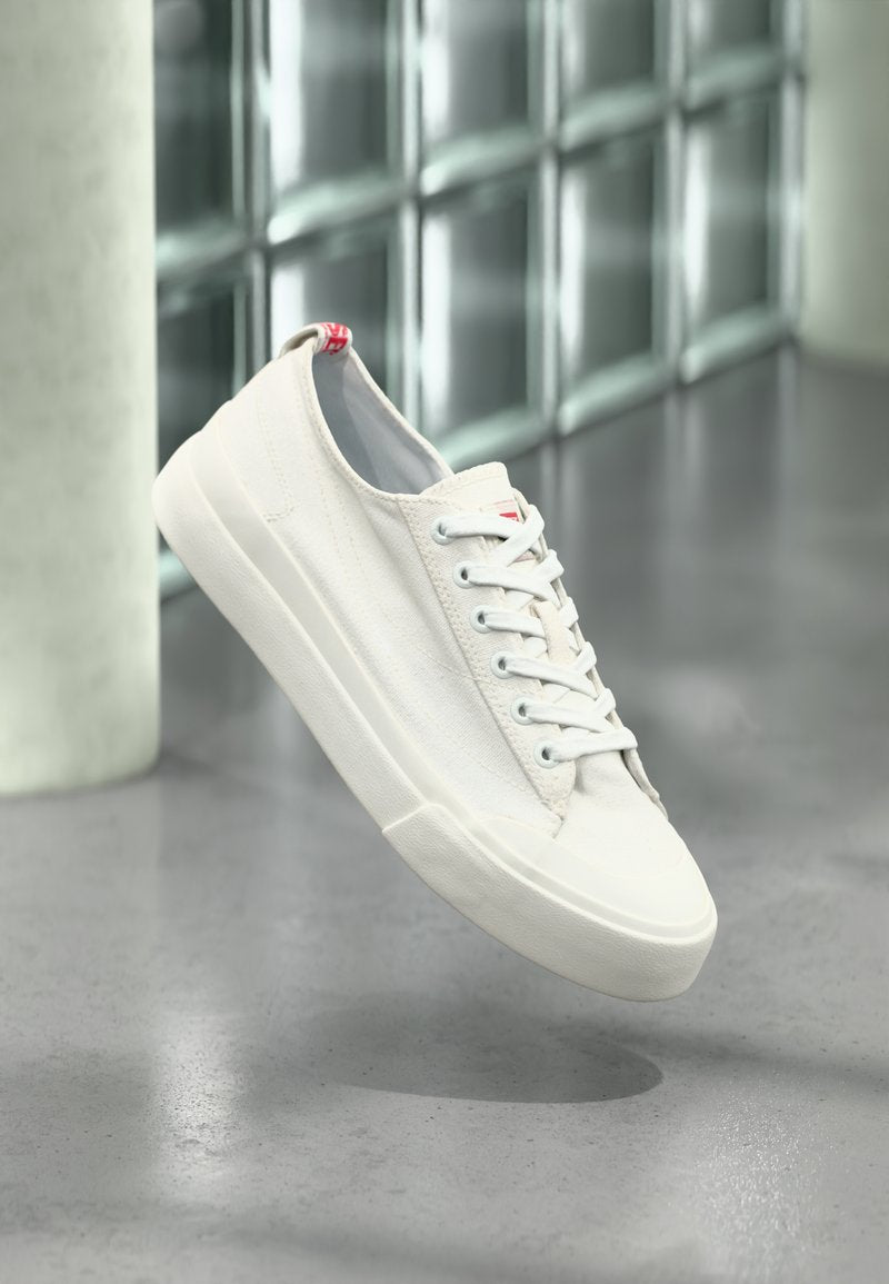 Weiße Leinenschuhe mit glatter Oberfläche, runder Zehenkappe und flacher Gummisohle. Schnürsenkel, Ösen und ein rotes Etikett verleihen markante Details.