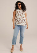 Ärmelloses, kragenloses Hemd mit einem beige- und braunfarbenen Palmenblattmuster; kombiniert mit hochgekrempelten hellblauen Jeans und beigen Keilsandalen.