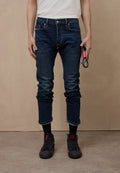 Dunkelblaue Jeans mit schmaler Passform, umgeschlagenen Säumen, Fünf-Taschen-Design und dezenten Ausbleichungen. Kombiniert mit schwarzen und roten Turnschuhen.