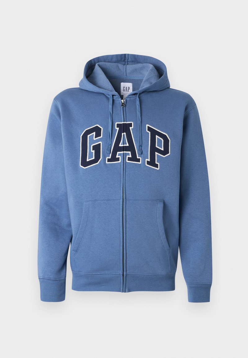 Blauer Kapuzenpullover mit Reißverschluss, Fronttaschen, Kordelzugkapuze und großen "GAP"-Buchstaben in Marineblau und Weiß über der Brust.