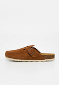 Brauner Veloursleder-Slipper mit verstellbarem Riemen und Korksohle, der auf einer flachen weißen Oberfläche liegt.