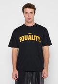 Junger Mann trägt ein schwarzes T-Shirt mit fettem gelbem Schriftzug „GLEICHHEIT“ und einem kleinen Kronensymbol über den Buchstaben, steht vor einem schlichten Hintergrund.