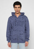Mann trägt einen blauen Kapuzenpullover mit Reißverschluss, verziert mit Paisley-Mustern und großen "GAP"-Buchstaben auf der Vorderseite, kombiniert mit hellblauen Jeans.