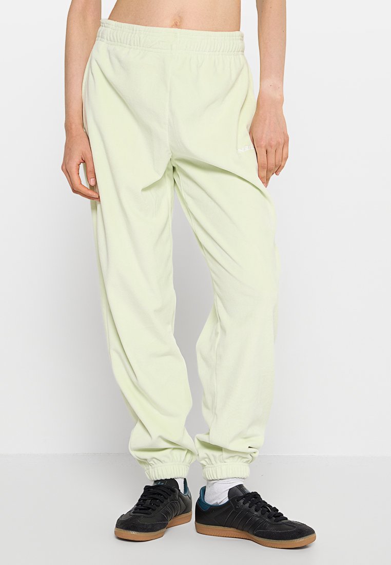 Hellgrüne, weiche Sweatpants aus Stoff mit einem elastischen Bund, gerippten Bündchen und einem weißen Logodetail. Getragen mit schwarzen Sportschuhen.
