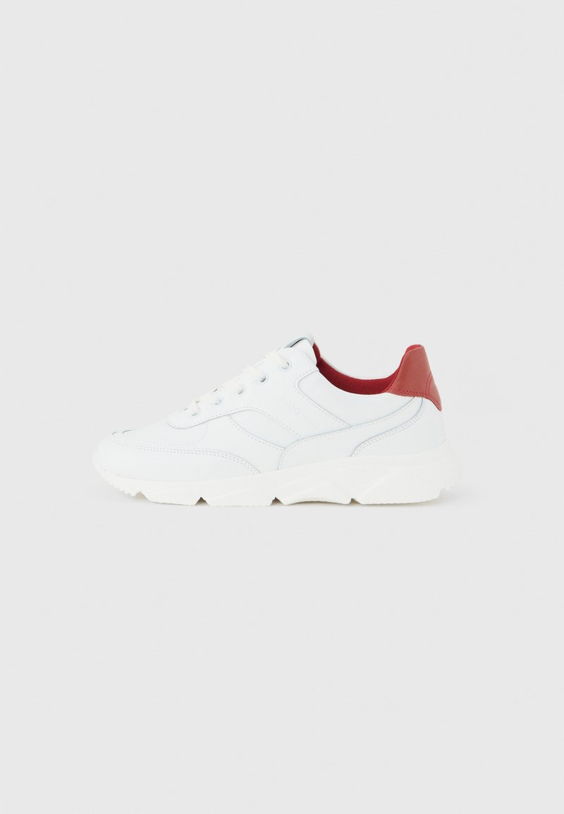 Weißer Sneaker mit klobiger Sohle, Schnürung vorne und rotem Fersenkragen, von der Seite auf einem schlichten hellgrauen Hintergrund gezeigt.