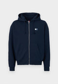 Dunkelblaue Zip-Hoodie aus weichem Stoff mit einer Vordertasche und einer Kapuze mit Zugband. Mit einem kleinen Logo-Patch auf der Brust.