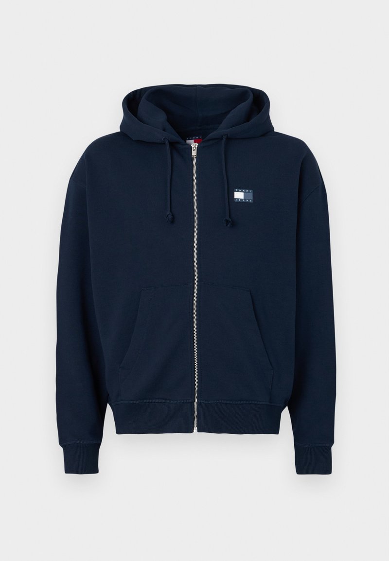 Dunkelblaue Zip-Hoodie aus weichem Stoff mit einer Vordertasche und einer Kapuze mit Zugband. Mit einem kleinen Logo-Patch auf der Brust.