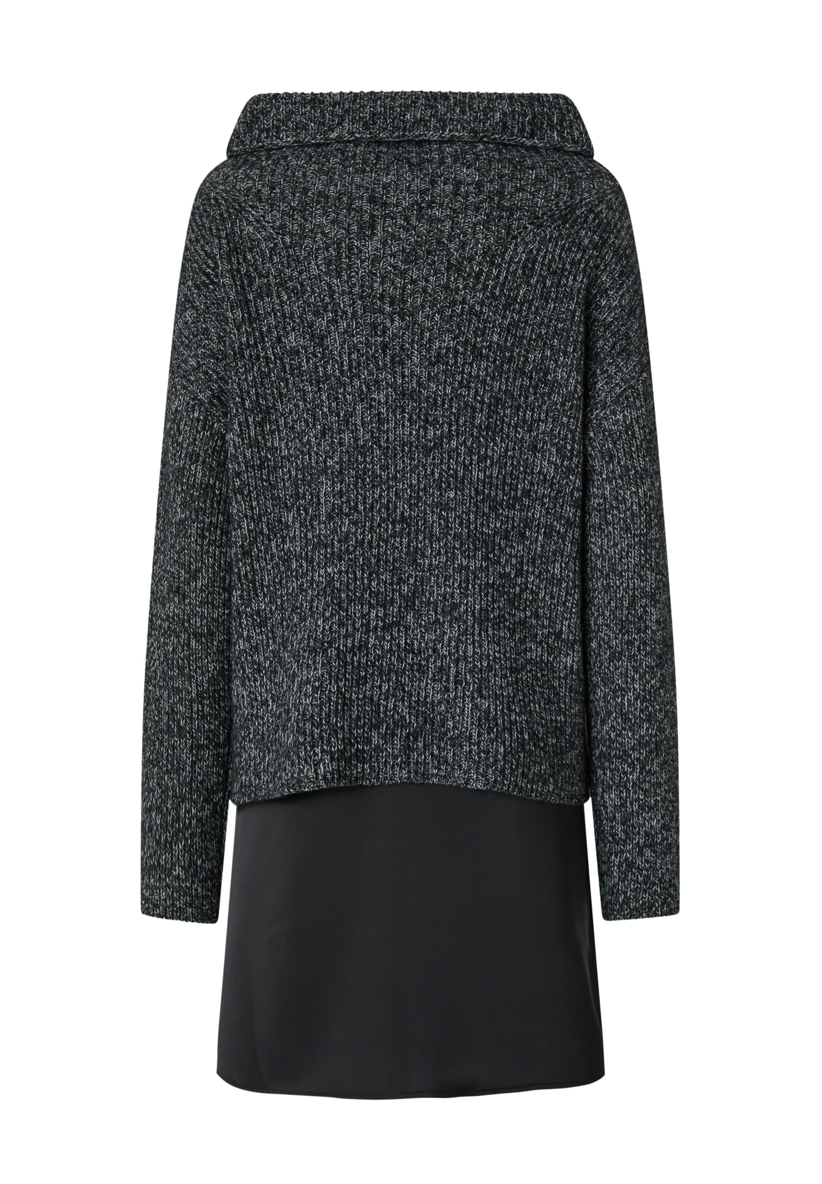 Dunkelgrauer Strickpullover mit weitem Kragen, geripptem Textur und lockerer Passform. Kombiniert mit einem glatten schwarzen Unterlayer, der unter dem Pullover hervorblitzt.