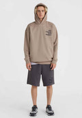 Beige Kapuzenpullover mit einem Frontlogo, kombiniert mit dunkelgrauen Shorts, die dasselbe Logo zeigen. Das Modell trägt graue Sneakers.