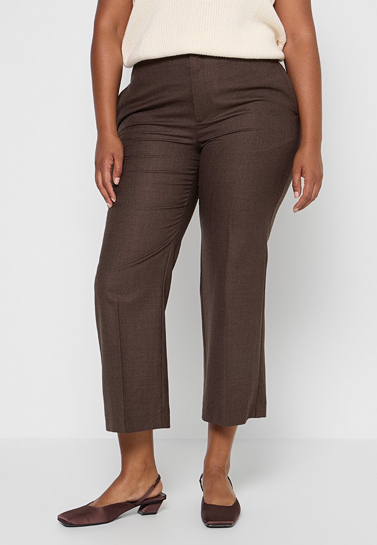 Braune, maßgeschneiderte Hose mit glatter Textur, mittlerer Bundhöhe und geradem Schnitt. Kombiniert mit dunkelbraunen Slippern.