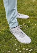 Hellgraue Sportschuhe mit strukturierten Flächen und Schnürsenkeln, kombiniert mit hellblauen Sporthosen, die auf einem mit kleinen Blumen bewachsenen Grasboden stehen.