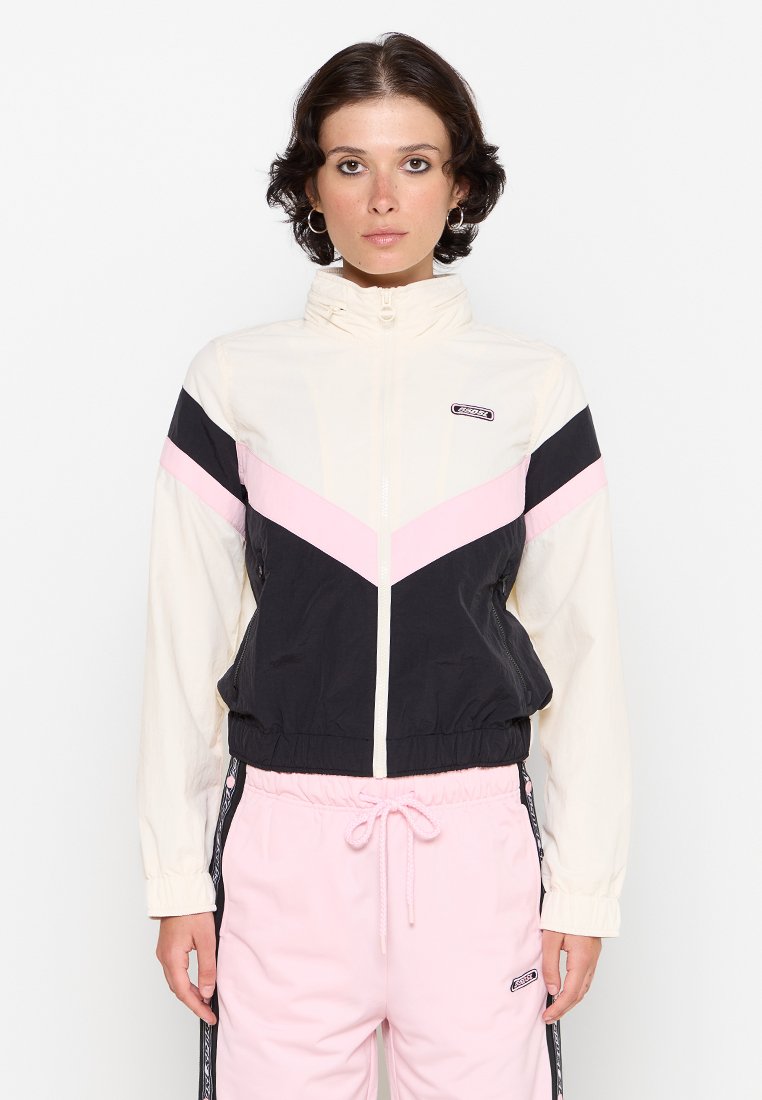 Windbreaker-Jacke mit einem Farbschnitt in Weiß, Schwarz und Pink, einem Reißverschluss vorne und elastischen Bündchen. Kombiniert mit rosa Sweatpants.