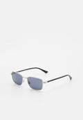 Rechteckige Sonnenbrille mit silbernem Metallrahmen, dunkelblauen Gläsern und schwarzen Bügeln, die auf einer weißen Oberfläche liegt.