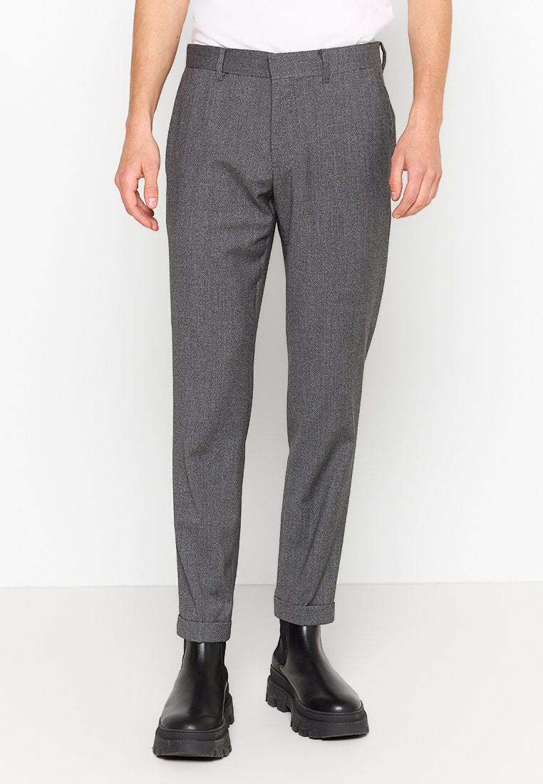 Grau gemusterte Hose mit taillierter Passform, schmalem Schnitt, seitlichen Taschen und umgeschlagenen Säumen, kombiniert mit schwarzen klobigen Stiefeln.