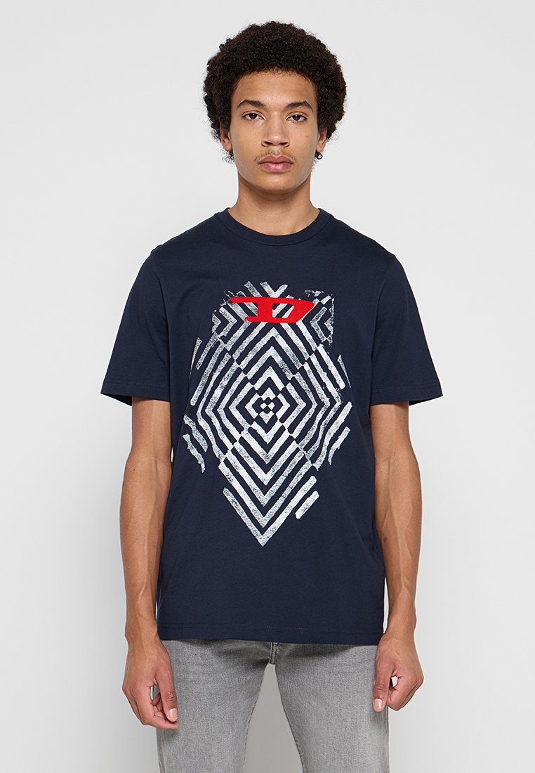 Marineblaues Baumwoll-T-Shirt mit einem geometrischen weißen und silbernen Muster, oben mit einem roten Akzent versehen. Kurzärmlig und mit Rundhalsausschnitt.