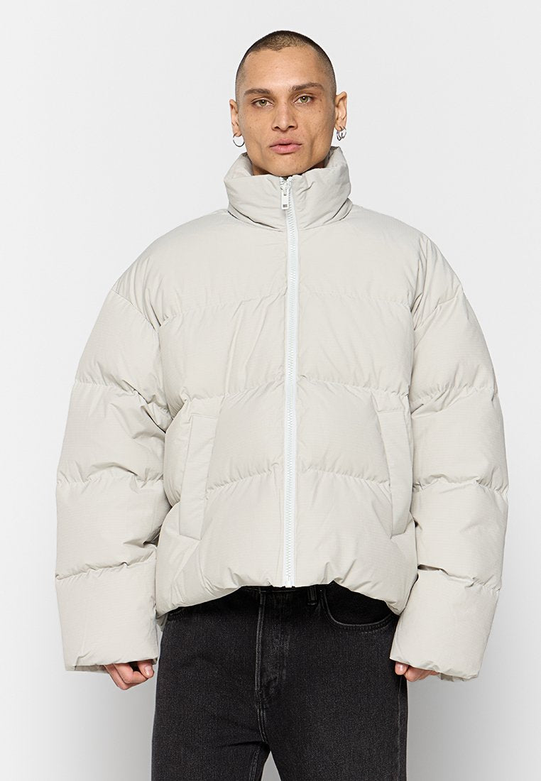 Beige gepolsterte Jacke mit hohem Kragen, Reißverschluss und weiten Ärmeln. Verfügt über ein diagonales Steppmuster und Fronttaschen.