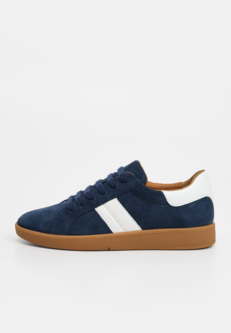 Marineblaue Wildledersneaker mit weißen Streifen, weißem Fersenpatch, braunem Innenfutter und Gummisohle, seitlich dargestellt.