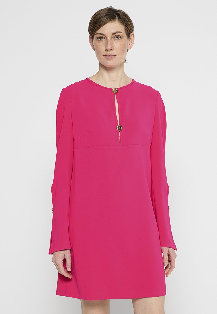 Kurzes pinkes Kleid mit langen, fließenden Ärmeln und einem Schlüssel-Ausschnitt, verziert mit goldenen Knopf-Akzenten und einem glatten, strukturierten Stoff.