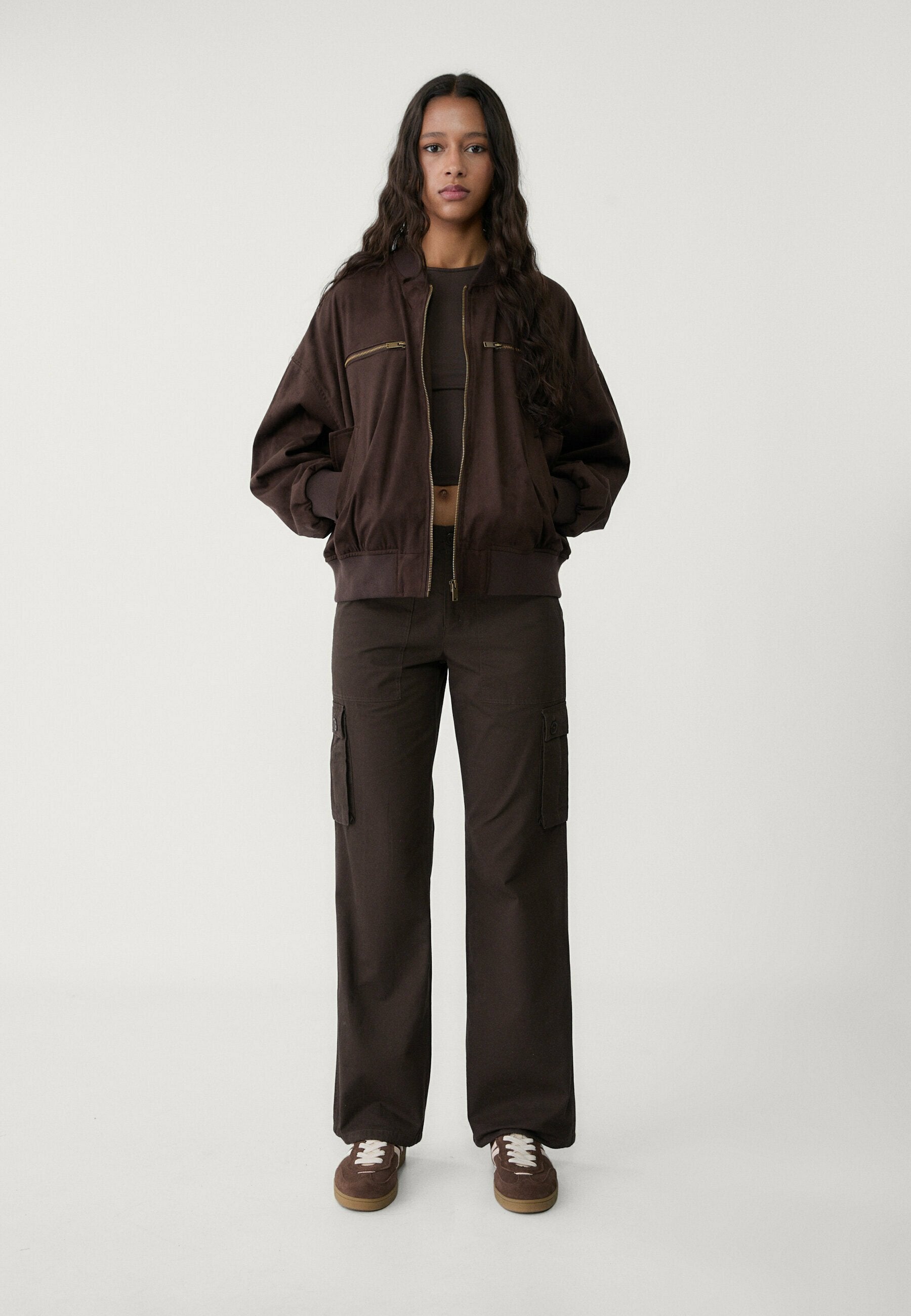 Braune Bomberjacke mit Reißverschlusstaschen, kombiniert mit passenden Cargo-Hosen mit Seitentaschen. Braune Sneaker vervollständigen das Outfit.