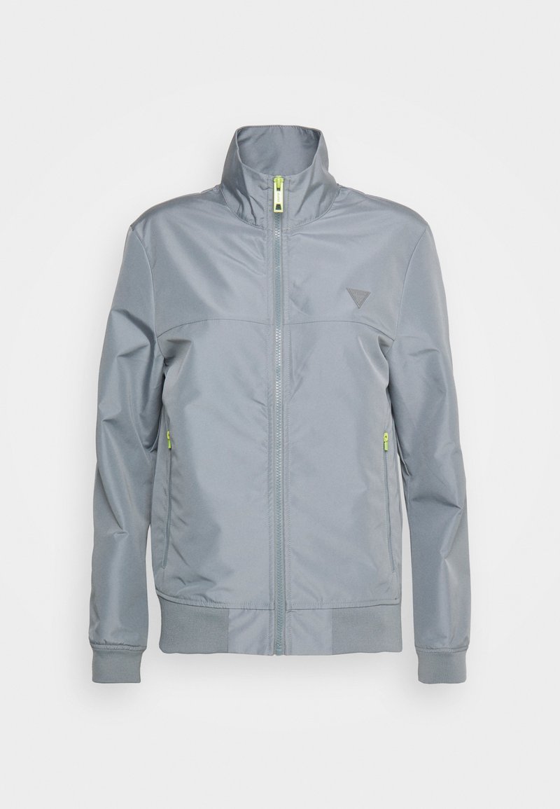 Graue Zip-Jacke mit hohem Kragen, ausgestattet mit einem dreieckigen Logo, gerippten Bündchen und leuchtend grünen Akzenten am Reißverschluss und den Taschen.