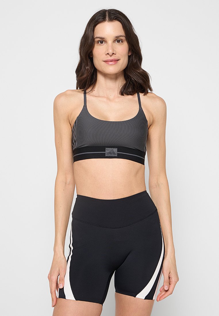 Schwarzer, gerippter Sport-BH mit dünnen Trägern und einem horizontalen Band am unteren Rand. Kombiniert mit hoch taillierten schwarzen Shorts mit weißen Akzenten.