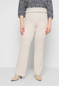 Frau trägt beige Textilhose mit hohem Bund und umgeschlagener Taille, kombiniert mit beigen spitzen Pumps und einer gemusterten Bluse.