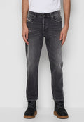 Mann in ausgebleichten schwarzen Jeans mit leichtem Used-Look und schwarzen Schnürstiefeln mit braunen Sohlen, entspannt mit den Händen stehend.