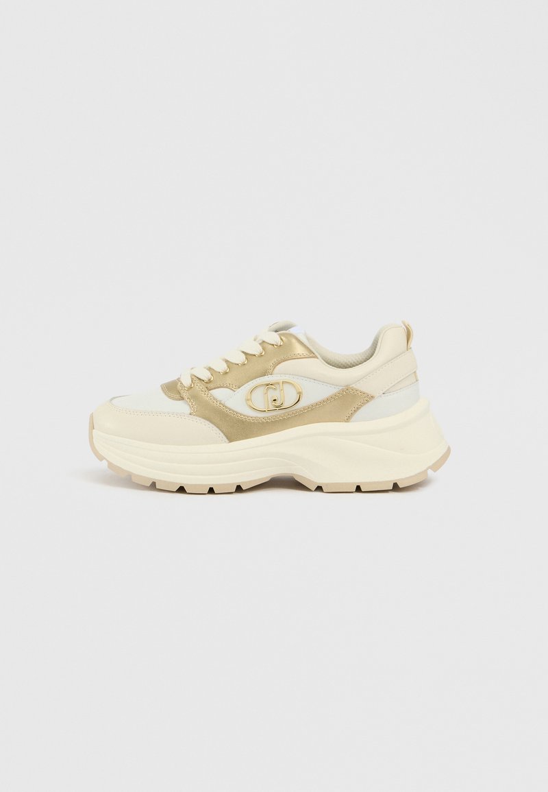 Creme- und goldfarbener Sneaker mit strukturiertem Obermaterial, klobiger Sohle, Schnürdesign und einem Logo-Akzent an der Seite.