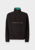 Schwarzer Fleecepullover mit hohem Kragen, vier schwarzen Druckknöpfen, grünem Innenkragen und "TOMMY JEANS" Schriftzug mit Logo auf der Brust.