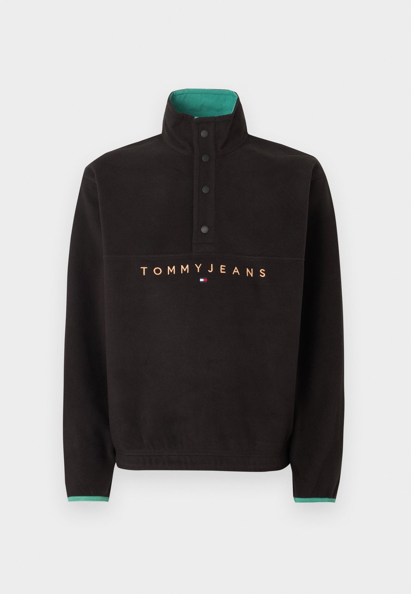 Schwarzer Fleecepullover mit hohem Kragen, vier schwarzen Druckknöpfen, grünem Innenkragen und "TOMMY JEANS" Schriftzug mit Logo auf der Brust.