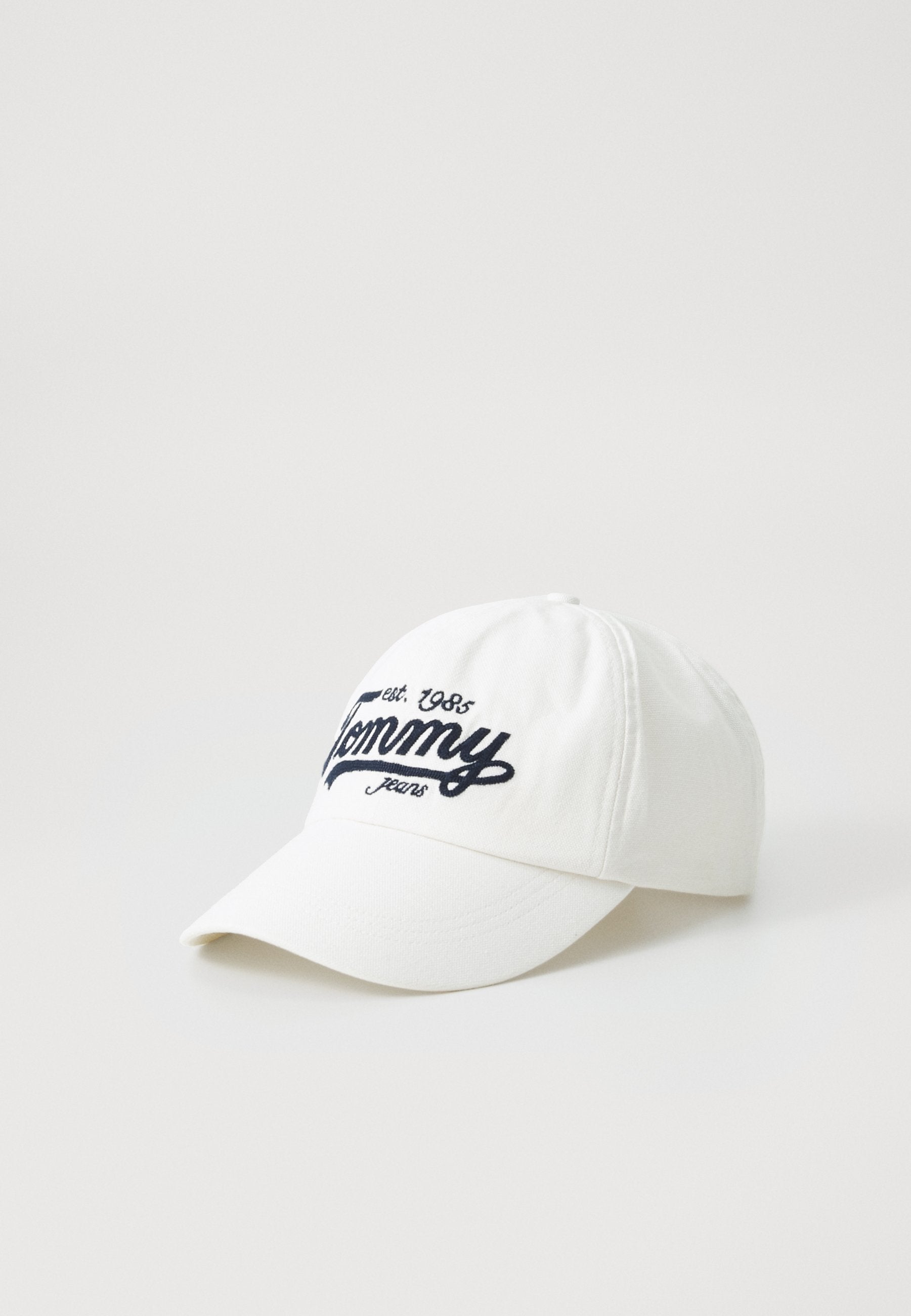 Weiße Baumwollmütze mit gebogenem Schirm und blauer gestickter Schrift "Tommy Jeans est. 1985." Einfaches Design ohne zusätzliche Verzierungen.