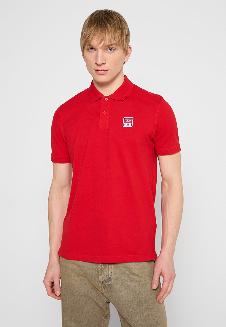 Rotes Poloshirt aus Baumwolle, mit einem Kragen und kurzen Ärmeln. Die Vorderseite zeigt ein kleines blau-weißes Logopatch. Figurbetonter Schnitt.