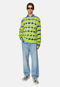 Grüner und blauer Batikpullover, der über einem blauen Hemd mit Kragen getragen wird, kombiniert mit hellblauen Jeans und gemusterten Sneakers.