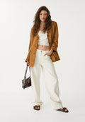 Brauner Wildleder-Overzise-Blazer, weißes Crop-Top, weite hellbeige Hose, braune Sandalen und eine dunkelbraune Handtasche. Lässiger und entspannter Schnitt.