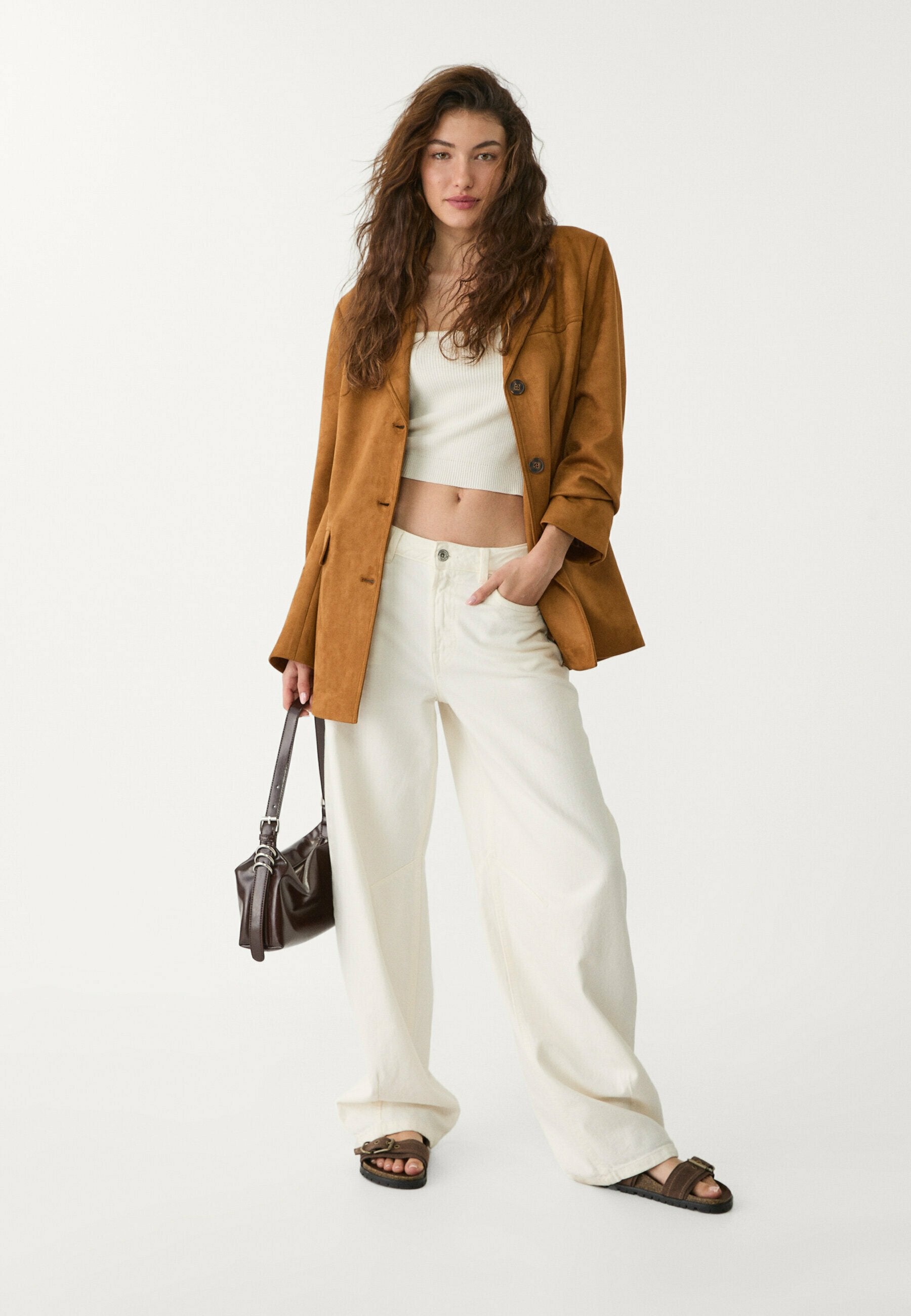 Brauner Wildleder-Overzise-Blazer, weißes Crop-Top, weite hellbeige Hose, braune Sandalen und eine dunkelbraune Handtasche. Lässiger und entspannter Schnitt.