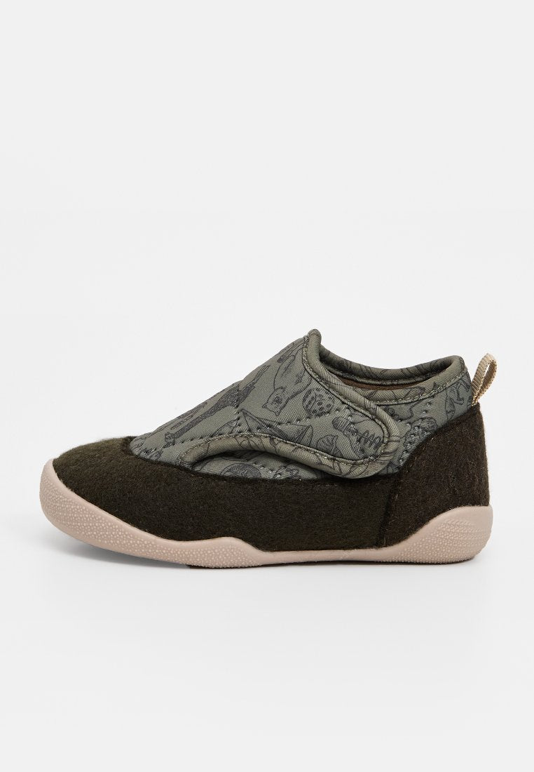 Grüne Slipper mit strukturierter Oberseite und einem dunkleren grünen Filzboden. Hervorhebung eines gemusterten Designs und einer beigen Gummisohle mit einer Schlaufe.