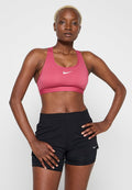Pinkes Sport-BH und schwarze Sportshorts. Der BH hat einen abgerundeten Ausschnitt und dünne Träger, mit einem kleinen weißen Nike-Logo. Die Shorts sind kurz und elastisch.