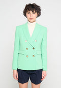 Mintgrüner, doppelt geknöpfter Blazer mit goldenen Knöpfen, Reverskragen und Vordertaschen, getragen über einem weißen Rollkragenpullover und blauen Shorts.