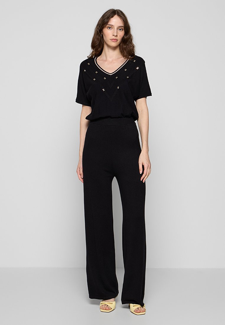 Schwarzes Lounge-Set bestehend aus einem V-Ausschnitt-Kurzarmoberteil mit dekorativen Verzierungen und weiten Hosen. Glattes Jersey-Material, lockere Passform.